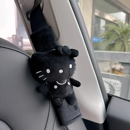 Black plush cat toy attached to a car seat belt in a vehicle.